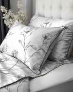 White bedding with black floral-embroidered pillowcase patterns on a bed.