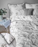 Bed with white duvet and pillows printed with black botanical lines; plant and open book on a nearby round table.