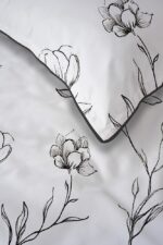 White bedding featuring a black, line-drawn floral pattern with a folded edge and dark piping.