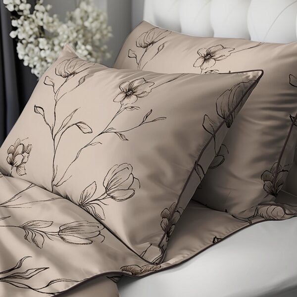 Beige satin pillowcases and quilt with black floral embroidery on a bed near a tufted white headboard, with white flowers in the background.
