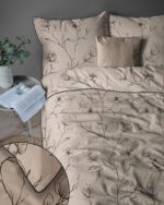 Beige duvet and pillows with black floral pattern on a bed; side table with plant, glass, and open book beside it.