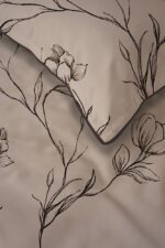 Beige bedsheet with a black embroidered floral vine pattern and a folded corner of a pillowcase.