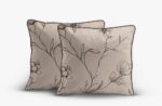 Two beige decorative pillows with black botanical embroidery and dark piping edges.