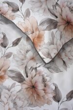 Close-up of a floral print with peach and gray peonies and leaves on white fabric, seam edge visible.