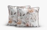 Pair of square decorative pillows with peach and gray floral pattern and dark piping edges.