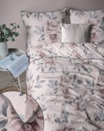 Bed made with blush-p pink floral duvet cover and matching pillow shams, plus a small gray decorative pillow, bedside table with a book and plant nearby