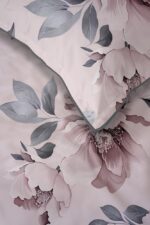 Close-up of pink floral bedding with large peony blossoms and grey-green leaves, a folded corner exposing the lighter underside.