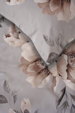 Close-up of light gray bedding with large pink-beige flowers and gray leaves, accented by a blue-gray edge.