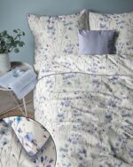 Bed with cream floral duvet and matching pillows in blue‑purple tones; a lavender pillow sits at the headboard.