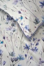 White fabric with a delicate pastel floral pattern in blues and purples, shown folded to reveal the light blue edge.
