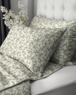 Cream-colored pillowcases with blue and yellow floral pattern on a bed with a white tufted headboard in the background.