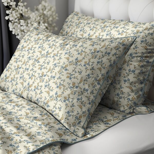 Cream-colored pillowcases with blue and yellow floral pattern on a bed with a white tufted headboard in the background.