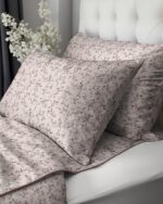 Soft pink floral bedding on a bed with matching pillowcases and quilted coverlet, against a white tufted headboard.