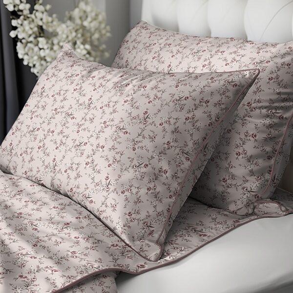 Soft pink floral bedding on a bed with matching pillowcases and quilted coverlet, against a white tufted headboard.