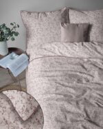 A bed with a pink floral duvet and matching pillows, a small round table with a plant, an open book, and a glass beside it.