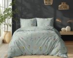 Bed with light blue floral duvet and matching pillows in a modern bedroom beside a tall plant.